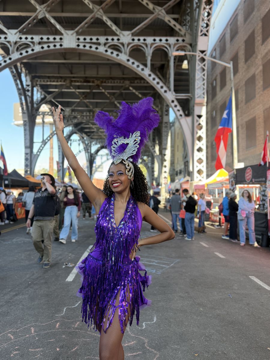 A samba dancer in purple feathers posing on 12th Ave under the viaduct